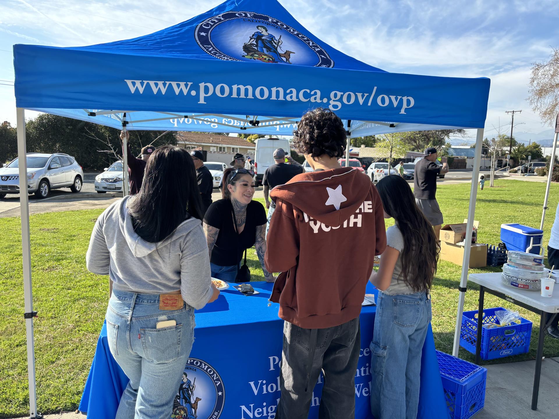 office of violence prevention staff spreading awareness, people standing around the pop up tent looking to gain more information, grassy field behind the tent