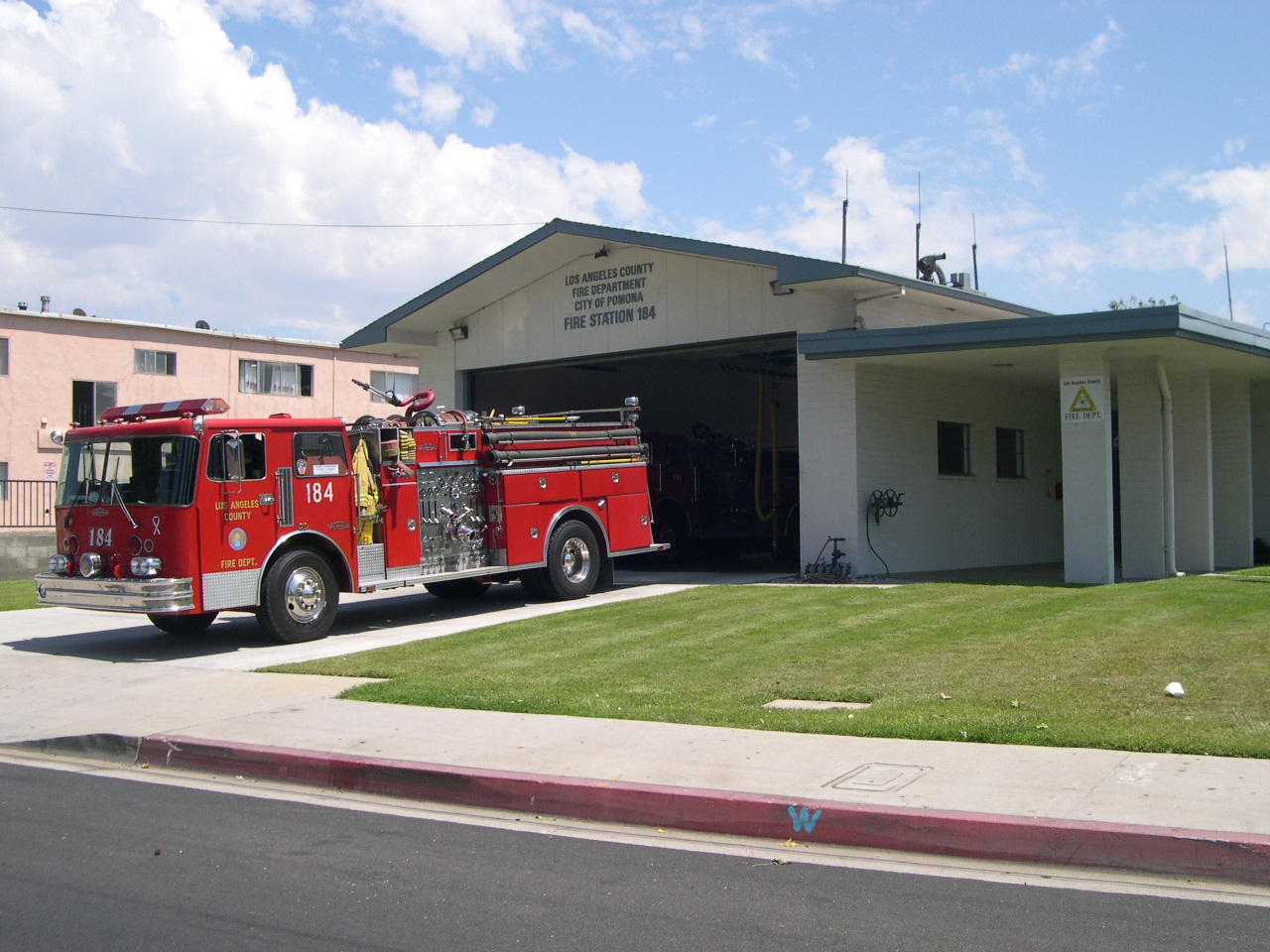 firetruck 184 parked outside of its 184 station. Beautiful grass and clear skies surround the truck